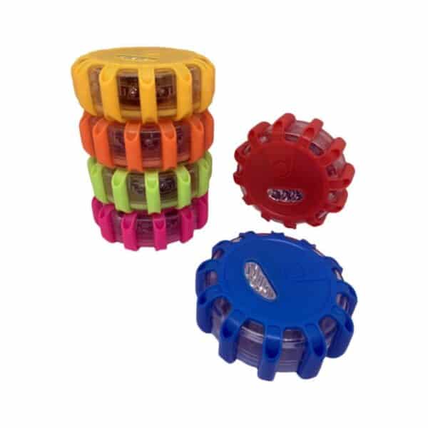 Four stacked circular LED road flares in yellow, orange, green, and pink; red and blue flares placed beside.