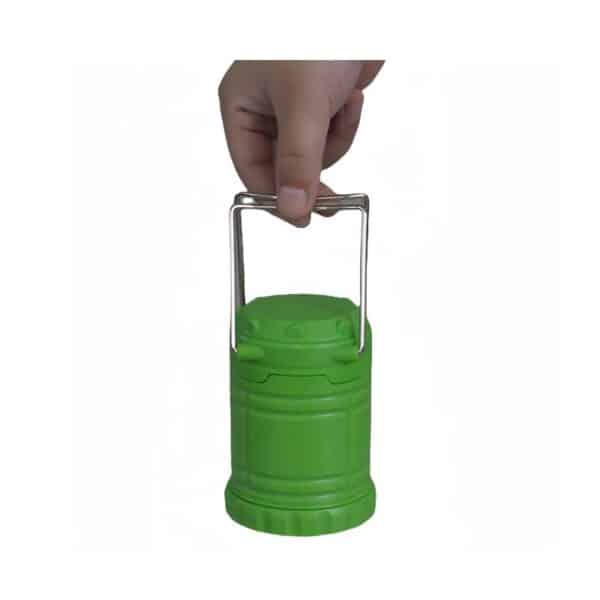 A hand holding a small green collapsible lantern by its silver handle.