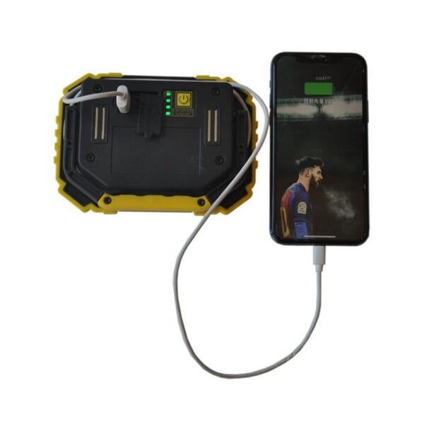 A smartphone, connected to a rugged power bank via cable, shows a charging icon on its screen.