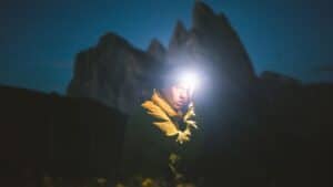 A person in a yellow jacket and headlamp stands outside at dusk, with blurred mountains in the background.