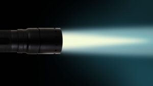 A black flashlight shines a bright beam to the right against a dark background.