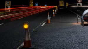 Cones and warning lights on dark highway at night, roadwork zone safety, traffic control, nighttime road maintenance, construction site with reflective safety equipment.