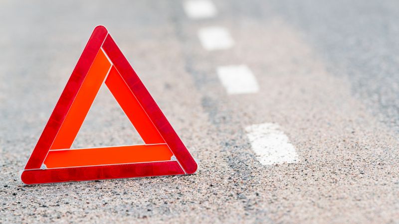 Reflective warning triangle on a gravel roadside, signaling vehicle breakdown or emergency situation.